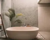 Elegante bañera exenta, rodeada de piedras blancas y una planta tropical. Muestra varios tipos de bañeras para un baño de lujo.