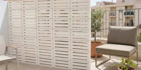 Muros cortina de bloques blancos con diseño de listones horizontales, creando un espacio exterior moderno con silla y plantas.