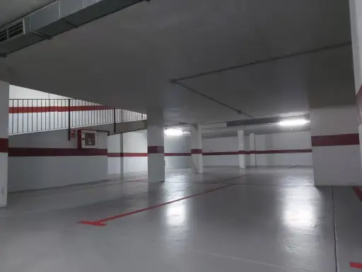 Suelo de garaje recién pintado, con líneas rojas y grises que marcan las plazas.