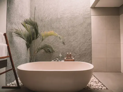 Relajante bañera exenta rodeada de piedras blancas, toallas dobladas en una escalera de madera y una planta tropical. Un ejemplo de cuartos de baño modernos y serenos.