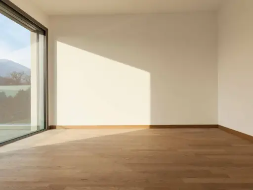 Habitación vacía con suelo de madera y grandes ventanas aislantes que ofrecen vistas a montañas y árboles.