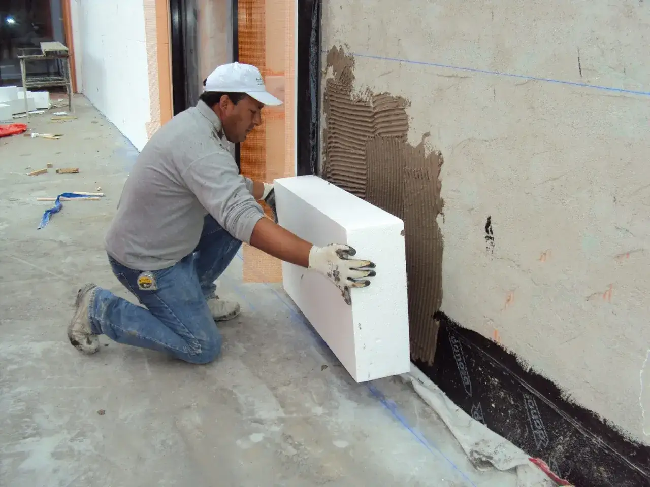 Obrero coloca pieza de aislante t&eacute;rmico exterior en pared.