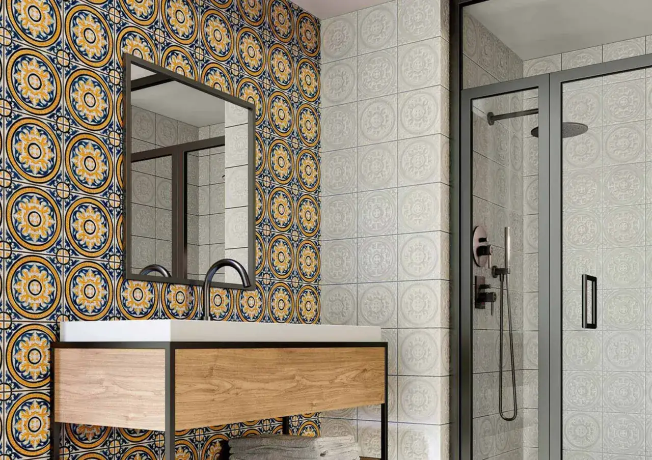 Baño pequeño con azulejos de estilo hidráulico en azul y amarillo vibrante en una pared, y azulejos blancos con relieve en otra.