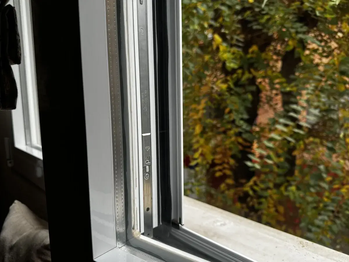 Marco de ventana blanco con detalles metálicos y vista a un árbol frondoso. El cristal Planitherm permite disfrutar del exterior.