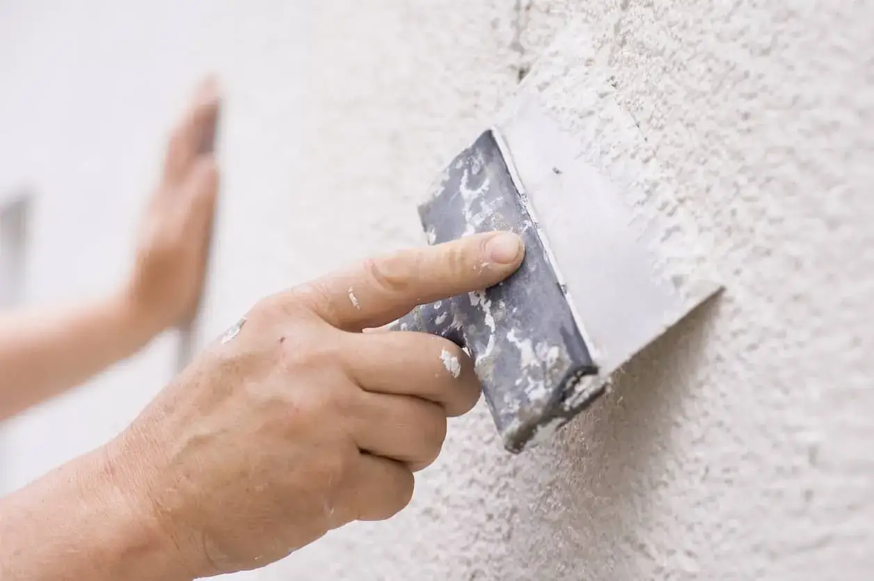 Mano aplicando masa con esp&aacute;tula para reparar gotele en pared texturizada.