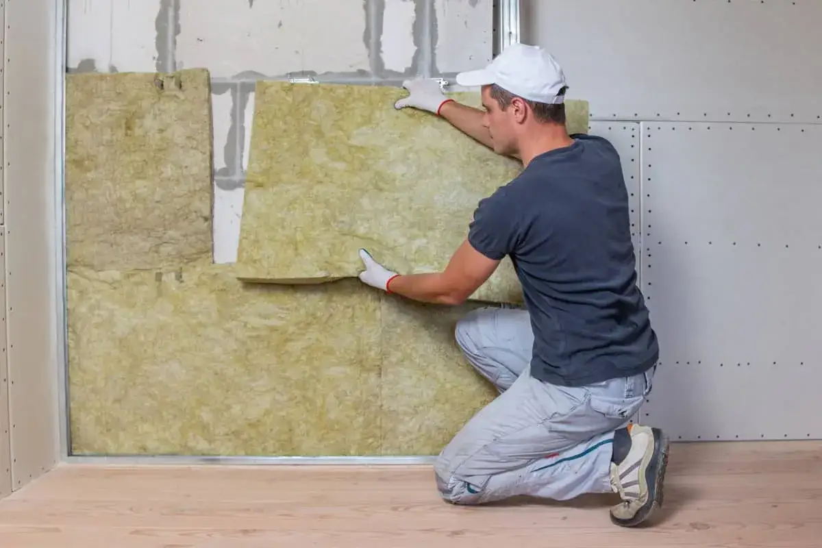Hombre instalando aislamiento en una pared. Aprende cómo aislar una pared para mejorar la eficiencia energética de tu hogar.