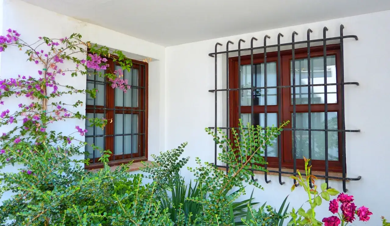 Ventanas de seguridad para casas con rejas de hierro forjado y enredaderas floridas.