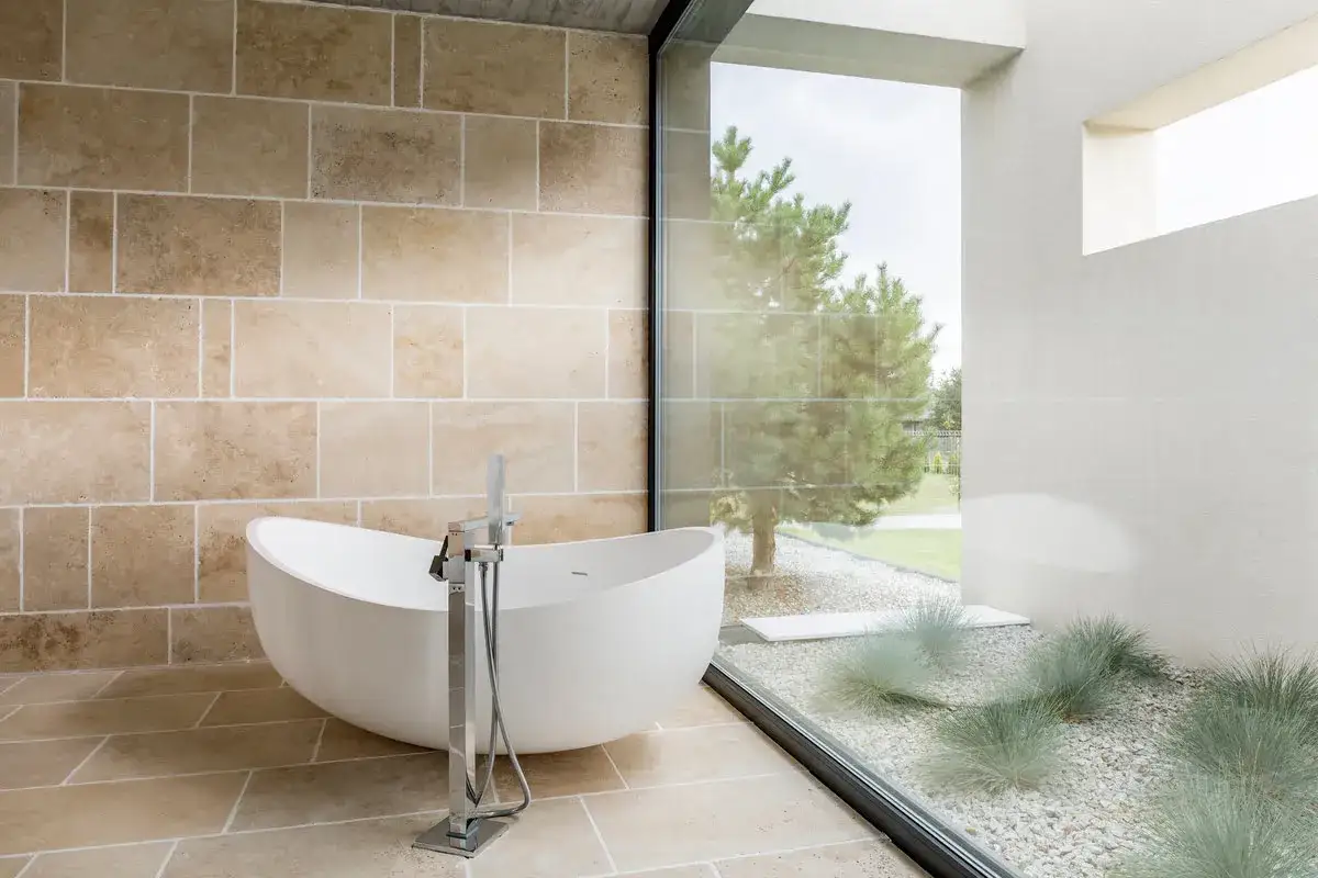 Un moderno ba&ntilde;o con ventana ofrece una ba&ntilde;era independiente y vistas a un jard&iacute;n con &aacute;rboles y c&eacute;sped.