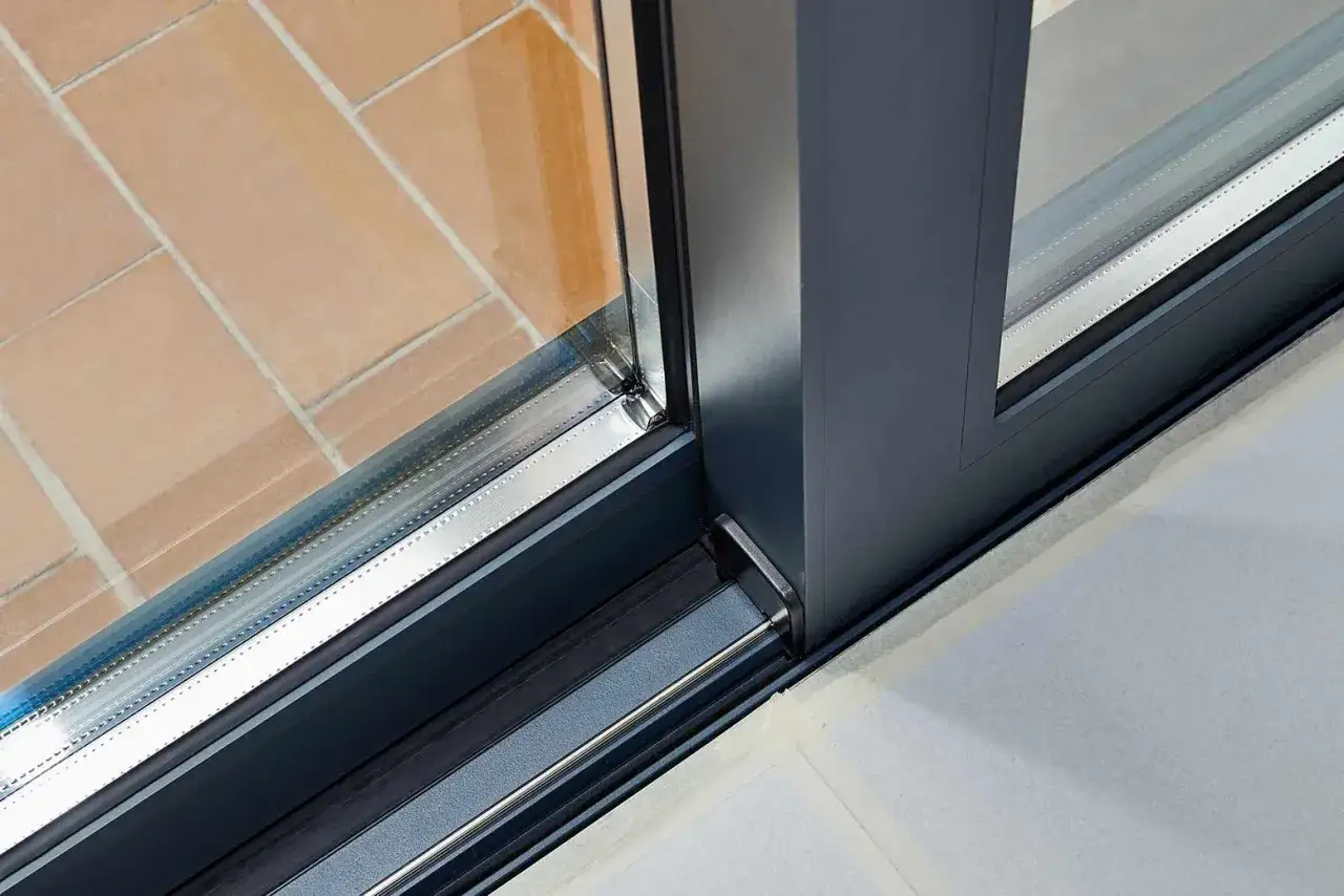 Detalle de ventana corredera con perfil oscuro y doble acristalamiento. Se observa un ejemplo de condensaci&oacute;n en el borde inferior del vidrio.