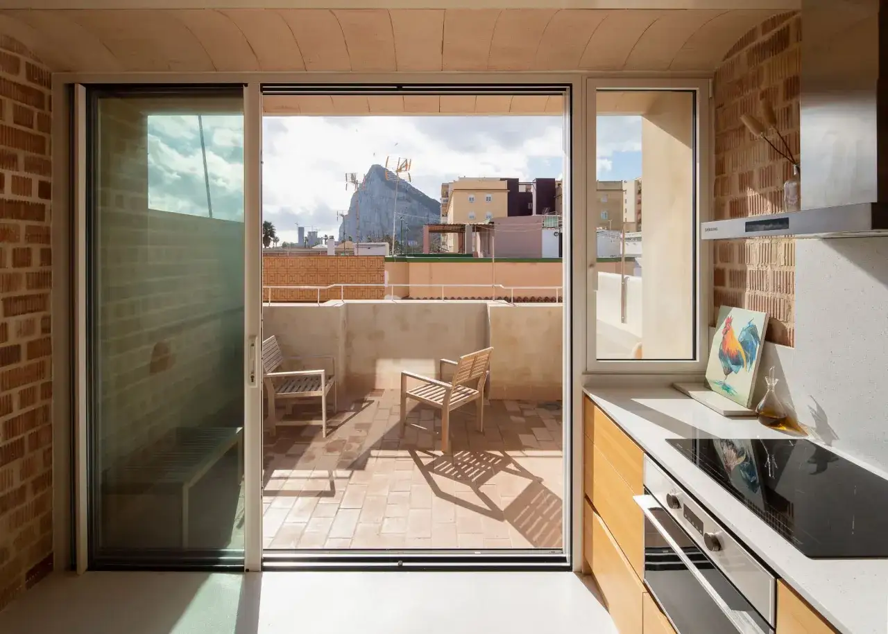 Cocina moderna con encimera de cuarzo y ventanas aislantes que dan a una terraza con vistas a un pe&ntilde;&oacute;n.