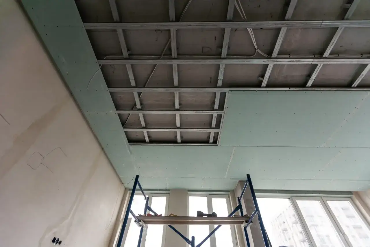 Instalación de falso techo de pladur para aislar techo ruido vecinos. Andamio y estructura metálica visibles.
