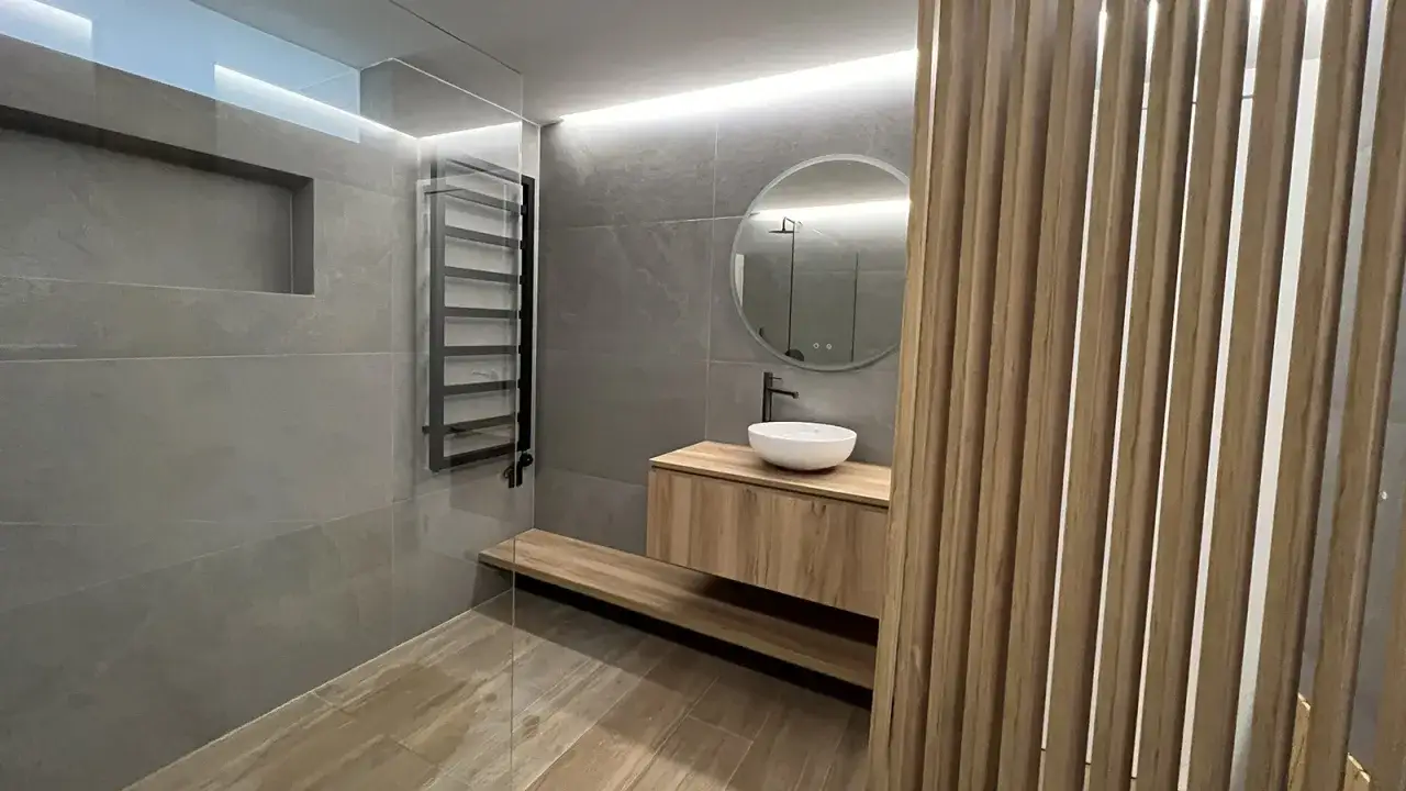 Modernos ideas ba&ntilde;os: lavabo sobre mueble de madera, espejo redondo, ducha con toallero negro y panel de lamas de madera.