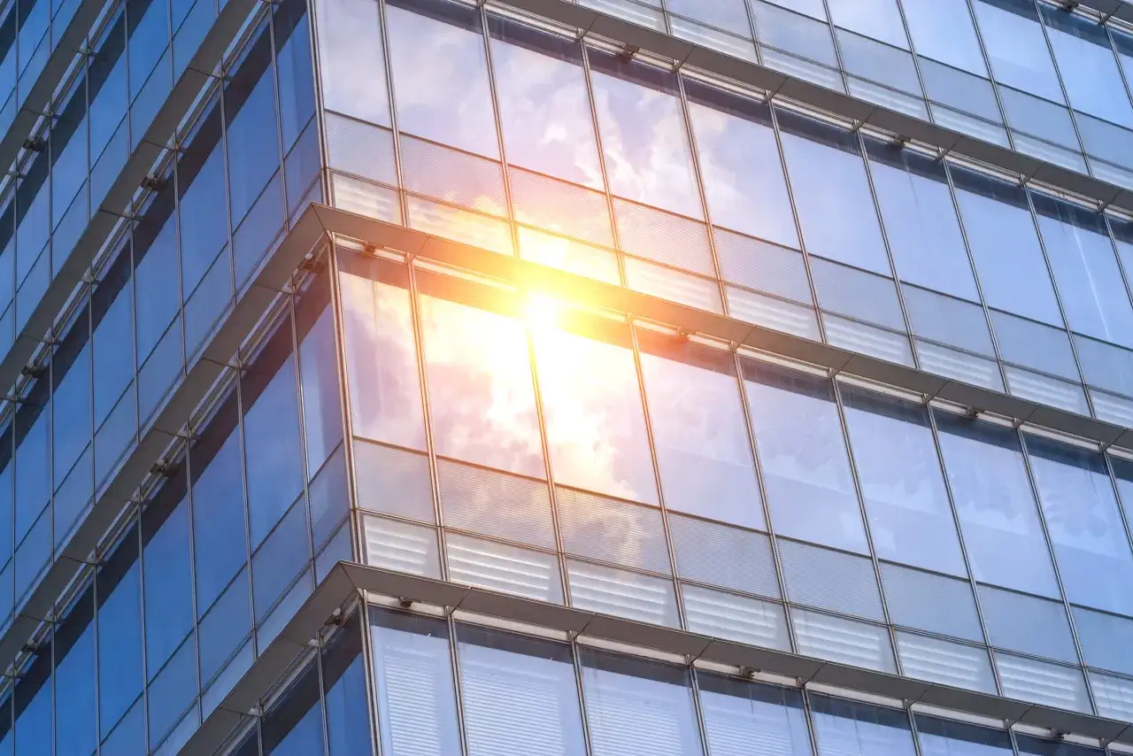 Edificio moderno con fachadas de solar glass que reflejan el cielo azul y el sol brillante.